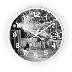 May include: Black and white clock featuring a photo of Nikola Tesla in his lab with a large electrical discharge. The clock face has white numbers and hands.