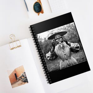 May include: A black and white photo of a woman wearing a large hat and holding a vintage camera to her face. The photo is printed on a spiral notebook.