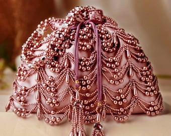 May include: A blush pink beaded drawstring bag. The bag is covered in small, round beads and larger teardrop-shaped beads. A matching drawstring and beaded tassels hang from the top. The bag has a soft, satin-like texture.