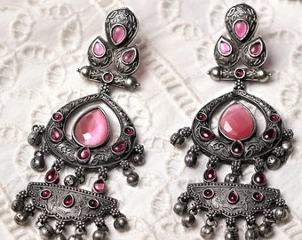May include: A pair of ornate silver-toned earrings with pink gemstones. Each earring features a teardrop-shaped central stone, smaller pink accents, and dangling silver beads. The earrings have an antique, vintage aesthetic.