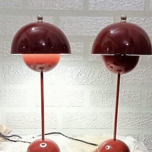 Puede incluir: Dos lámparas de mesa rojas con una pantalla en forma de hongo y una base redonda. Las lámparas están sobre una alfombra blanca y esponjosa.