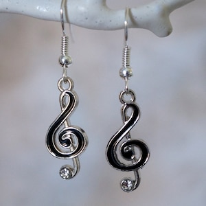 May include: A pair of silver earrings with black enamel treble clef charms and clear crystal accents.