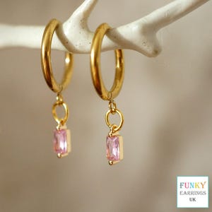 May include: Gold hoop earrings with a dangling pink square-shaped gemstone charm.