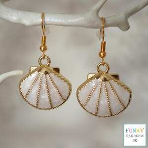 May include: Gold tone earrings with a white seashell design. The seashells have a textured surface and a gold trim.