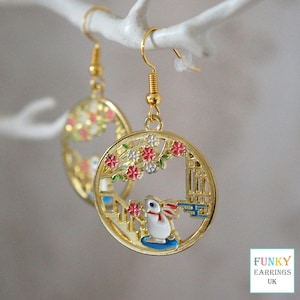 May include: Gold tone earrings with a white rabbit and pink and white flowers in a circular design.