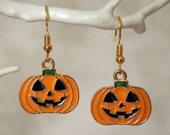 May include: A pair of gold pumpkin earrings with black eyes, a black smile, and a green stem. The pumpkins are orange and have a textured surface.