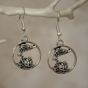 May include: Silver dangle earrings with a circular design featuring a bird perched on a branch. The earrings have a delicate, intricate design.