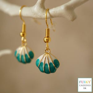 May include: Gold-coloured seashell earrings with white and teal enamel detailing. The earrings are suspended from a white branch. Each earring has a gold-coloured hook and a spring detail. The text "FUNKY EARRINGS UK" is in the bottom right corner.