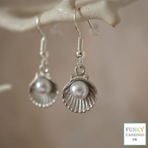 May include: Silver seashell earrings with a white pearl centre. The earrings are suspended from a white branch. The earrings have a fish hook style closure. The text "FUNKY EARRINGS UK" is in the bottom right corner.