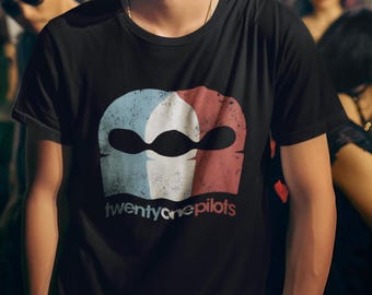 May include: A black crew neck t-shirt featuring a distressed graphic of a three-part logo in light blue, white, and red. Below the logo, the text twenty one pilots is printed in a matching color scheme with a weathered, worn-in texture.