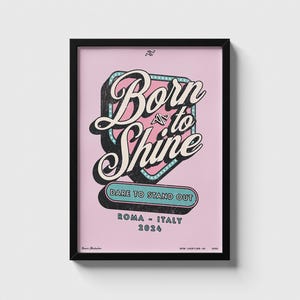 Può includere: Un poster incorniciato con le parole "Born to Shine" in un font retrò, su sfondo rosa. Il poster include la frase "Dare to Stand Out" e la località "Roma - Italy 2024". La cornice è nera.