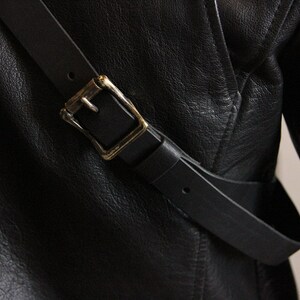 May include: A black leather jacket with a black leather strap and a gold buckle.