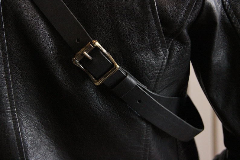 May include: A black leather jacket with a black leather strap and a gold buckle.
