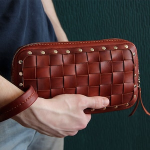 May include: A brown leather clutch with a woven design and gold studs. The clutch has a zipper closure and a small strap.