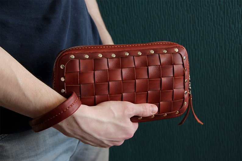 May include: A brown leather clutch with a woven design and gold studs. The clutch has a zipper closure and a small strap.