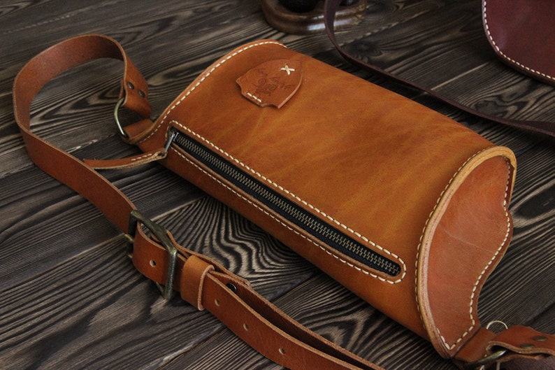 May include: A brown leather crossbody bag with a zipper closure and a small metal emblem. The bag has a long adjustable strap.