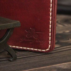 May include: Close-up of a burgundy leather wallet with white stitching. The wallet has a logo embossed on the front that says "yeway bay".