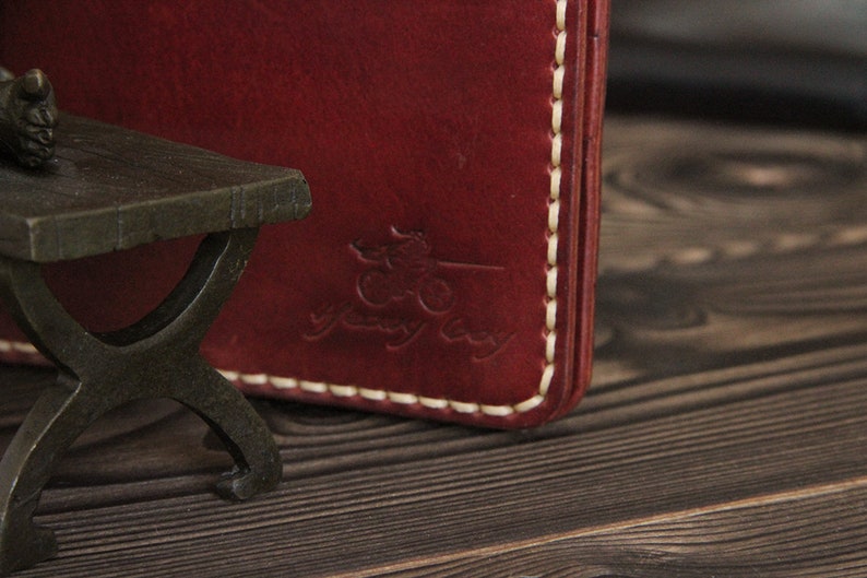 May include: Close-up of a burgundy leather wallet with white stitching. The wallet has a logo embossed on the front that says "yeway bay".