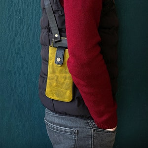 May include: A person wearing a red sweater and a black vest with a yellow leather phone case attached to the vest.