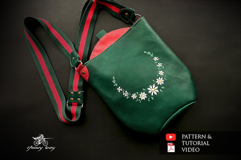 May include: A green leather crossbody bag with a red and green striped strap. The bag has a white daisy embroidery design. The bag is on a black background.  "PATTERN & TUTORIAL VIDEO"
