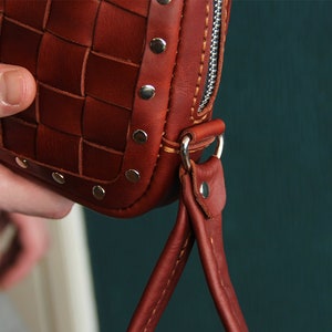 May include: A brown leather bag with a woven design and silver studs. The bag has a zipper closure and a short strap.