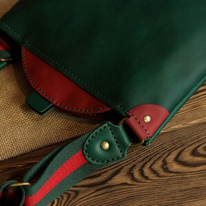 May include: A green leather crossbody bag with a red leather accent and a green and red striped strap.