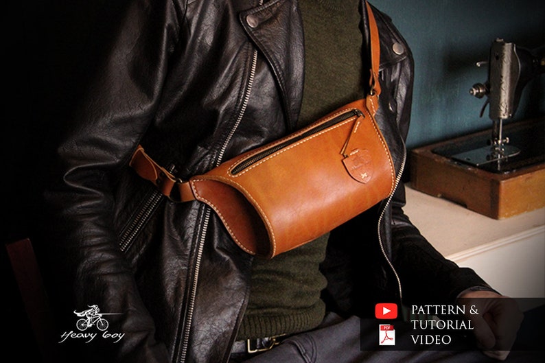 May include: A brown leather fanny pack with a zipper closure and a small leather flap with a logo. The bag is worn by a person wearing a black leather jacket.