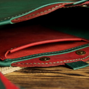 May include: A green leather purse with a red leather lining and a snap closure. The purse has a small pocket on the inside and a long strap.