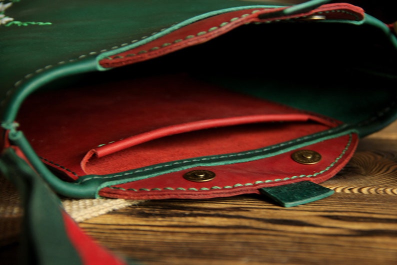 May include: A green leather purse with a red leather lining and a snap closure. The purse has a small pocket on the inside and a long strap.