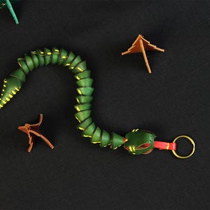 Op de afbeelding: Een groene leren slangen sleutelhanger met gele accenten en een rode en gouden sleutelring.