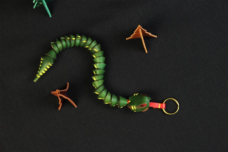 Op de afbeelding: Een groene leren slangen sleutelhanger met gele accenten en een rode en gouden sleutelring.