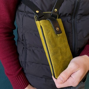May include: A yellow leather phone case with black stitching and a black strap. The case is worn over the shoulder.