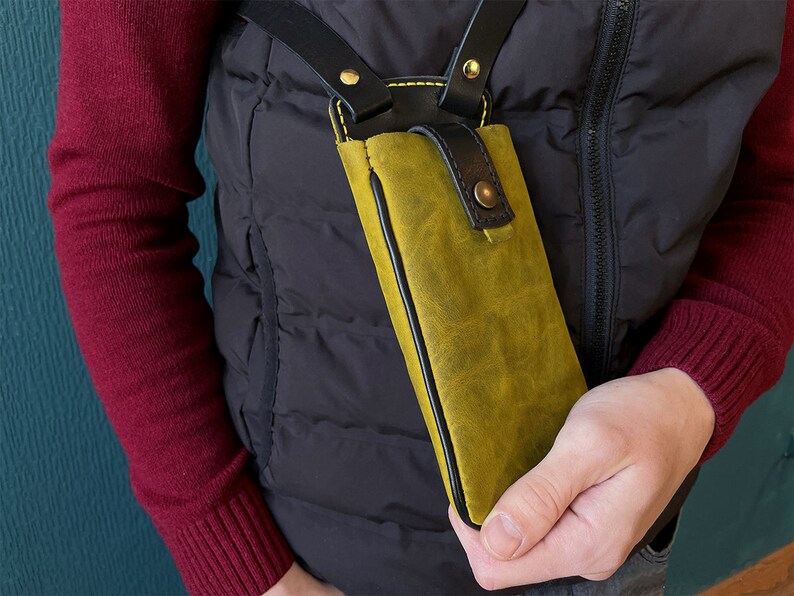 May include: A yellow leather phone case with black stitching and a black strap. The case is worn over the shoulder.