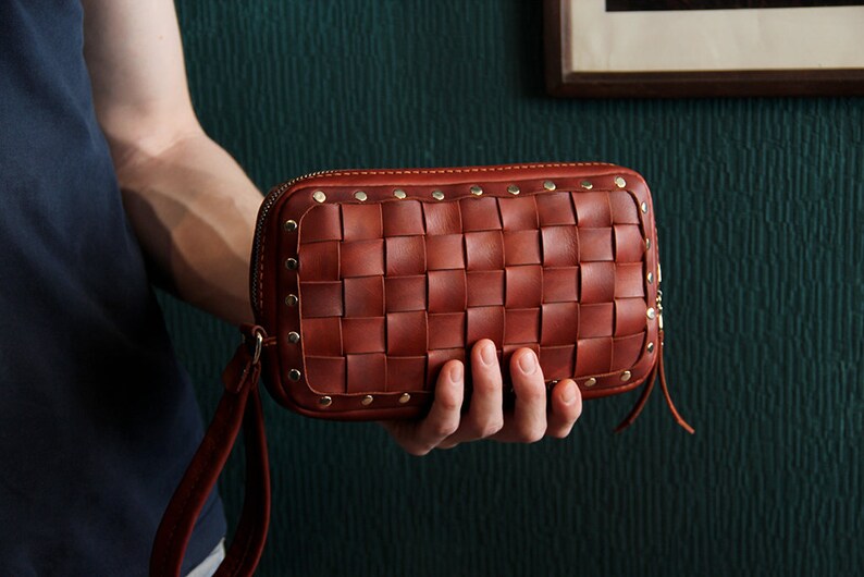 May include: A brown leather clutch with a woven design and gold studs. The clutch has a zipper closure and a strap.