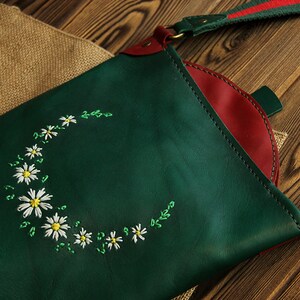 May include: A green leather crossbody bag with a red leather lining and a white daisy embroidery design.