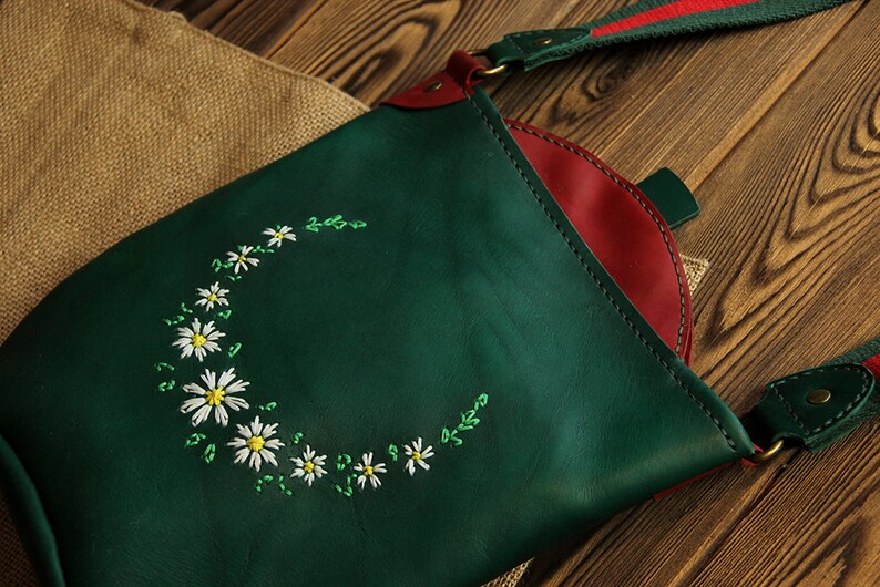 May include: A green leather crossbody bag with a red leather lining and a white daisy embroidery design.