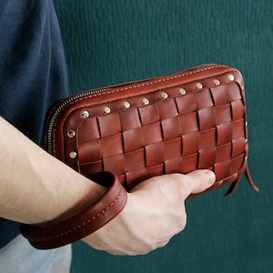 May include: A brown leather woven clutch with a zipper closure and silver studs. The clutch has a braided leather strap.