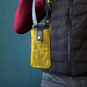 May include: A yellow leather phone case with a black strap. The case is worn over the shoulder and has a flap closure.
