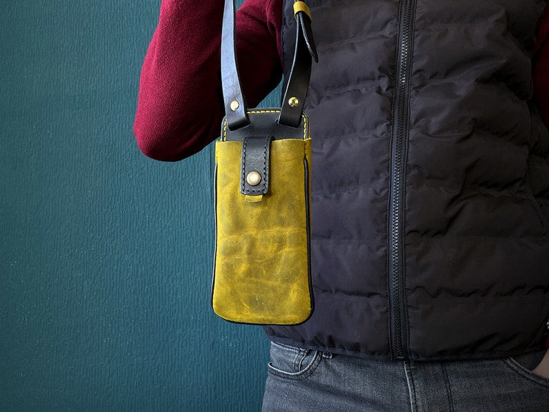 May include: A yellow leather phone case with a black strap. The case is worn over the shoulder and has a flap closure.