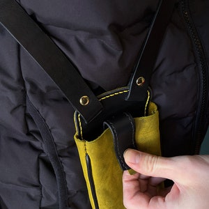 May include: A yellow leather phone case with black leather straps and gold accents. The case is attached to a black leather strap that goes over the shoulder.