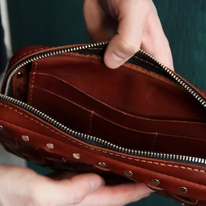 May include: A brown leather wallet with a zipper closure and multiple compartments. The wallet is open and the interior is visible.
