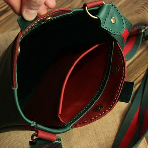 May include: Green leather crossbody bag with a red leather interior and a green and red striped strap.