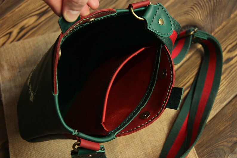 May include: Green leather crossbody bag with a red leather interior and a green and red striped strap.