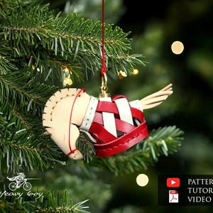 May include: A handcrafted Christmas ornament shaped like a horse, with a cream-colored head and red and white woven body. The ornament hangs from a red string on a Christmas tree. The background is blurred with bokeh lights.
