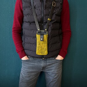 May include: A person wearing a black vest and red sweater with a yellow leather phone case attached to a black strap.