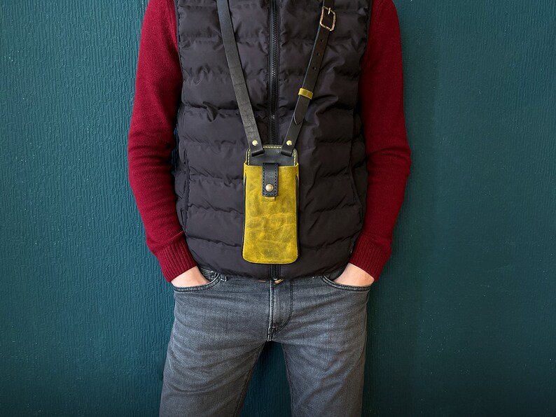 May include: A person wearing a black vest and red sweater with a yellow leather phone case attached to a black strap.