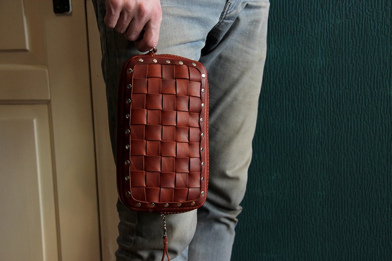 May include: A brown leather clutch bag with a woven design and silver studs. The bag has a zipper closure and a small tassel.