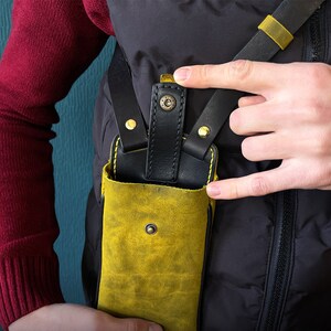 May include: A yellow leather phone case with a black leather strap and gold accents. The case is worn on a person's body.