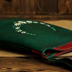 May include: A green leather shoulder bag with a red trim and a white daisy floral embroidery design.