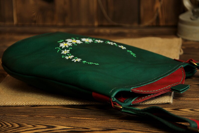 May include: A green leather shoulder bag with a red trim and a white daisy floral embroidery design.